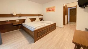 A bedroom with a wooden bed, bedside tables, a flat-screen TV, and a door leading to another room. - Alemannenhof Engel (Rickenbach)