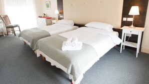 Une chambre d’hôtel avec deux lits, un bureau, une chaise et une table de chevet avec une lampe.