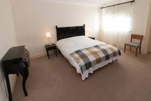 Quarto de hotel com uma cama, duas mesas de cabeceira, uma cadeira e uma escrivaninha.
