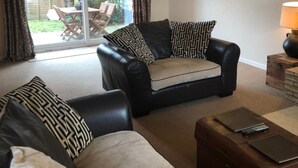 A living room with two sofas, a table, and a lamp. There is a sliding glass door leading to a patio with a table and chairs. - The Walnuts Country House (Bury St Edmunds)