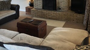 A living room with a brick fireplace, a sofa, a coffee table, and a television. - The Walnuts Country House (Bury St Edmunds)