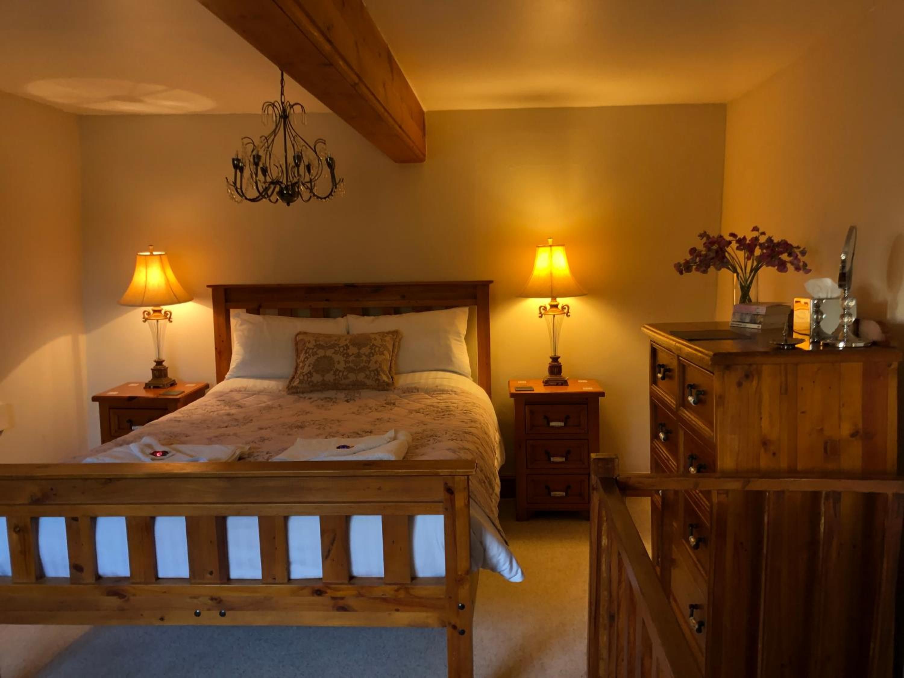 A bedroom with a wooden bed, two bedside lamps, a chandelier, and a wooden dresser with a mirror.