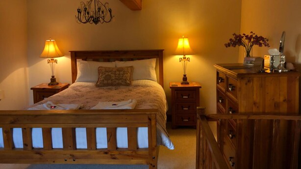 A bedroom with a wooden bed, two bedside lamps, a chandelier, and a wooden dresser with a mirror. - The Walnuts Country House (Bury St Edmunds)