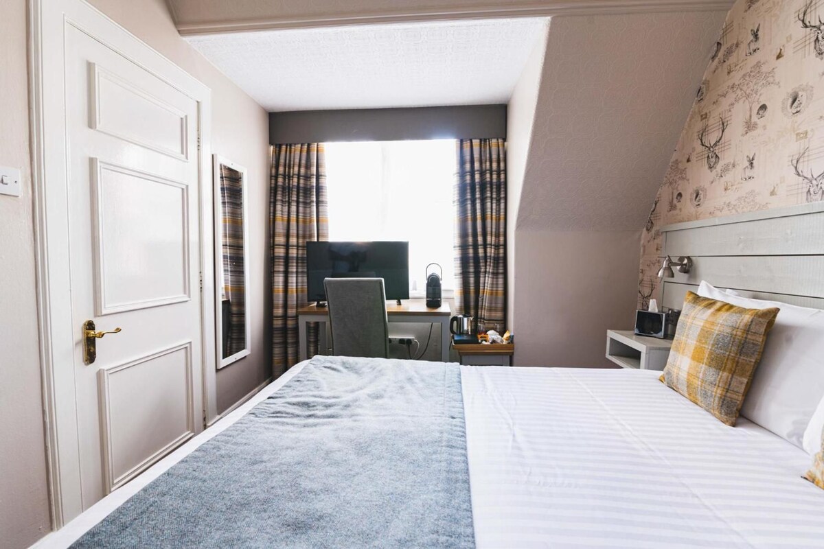 Habitación de hotel con cama, escritorio, computadora, silla y televisor.