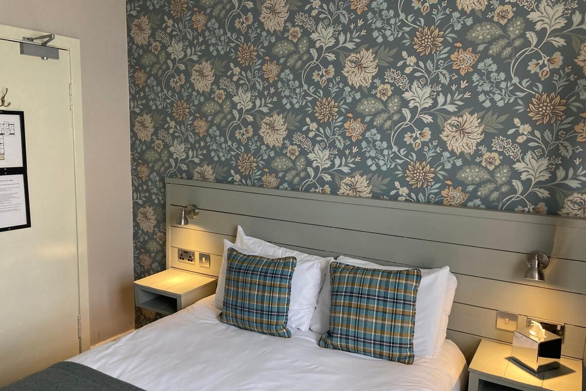 Et hotelværelse med en seng, to sengeborde, en natbord og en lampe på væggen.