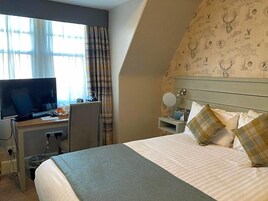 Habitación de hotel con cama, escritorio con televisor, silla, mesita de noche con lámpara y pared con diseño.