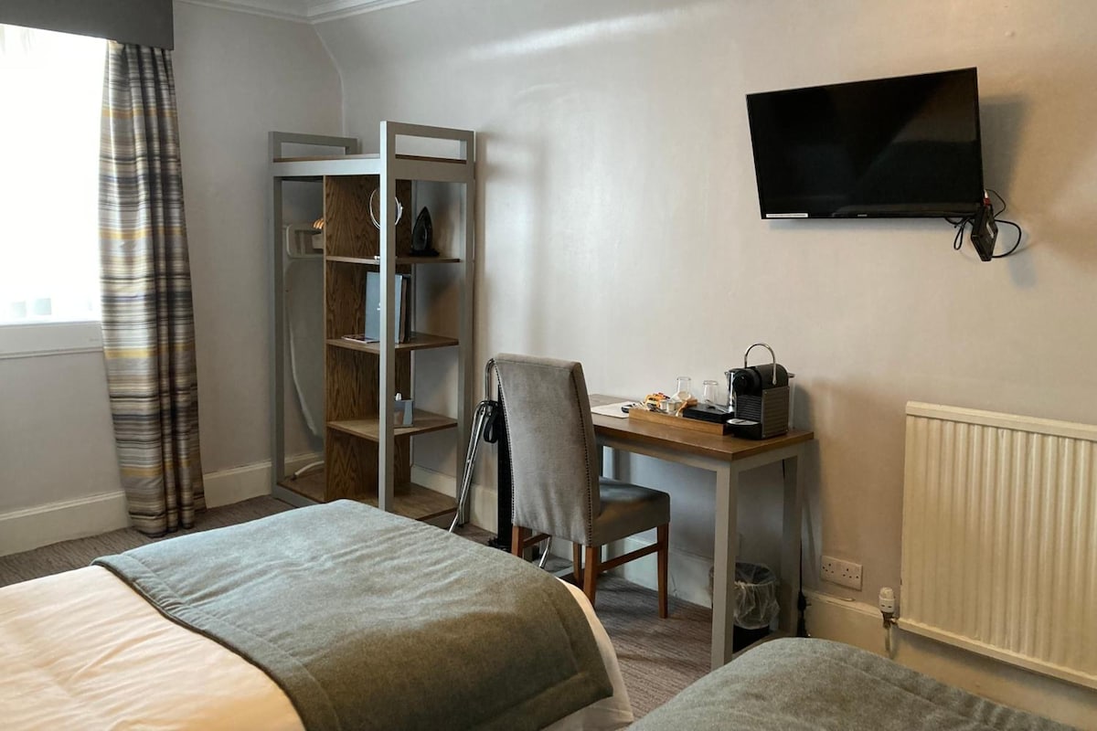 Habitación de hotel con dos camas, un escritorio con silla, televisión y armario.