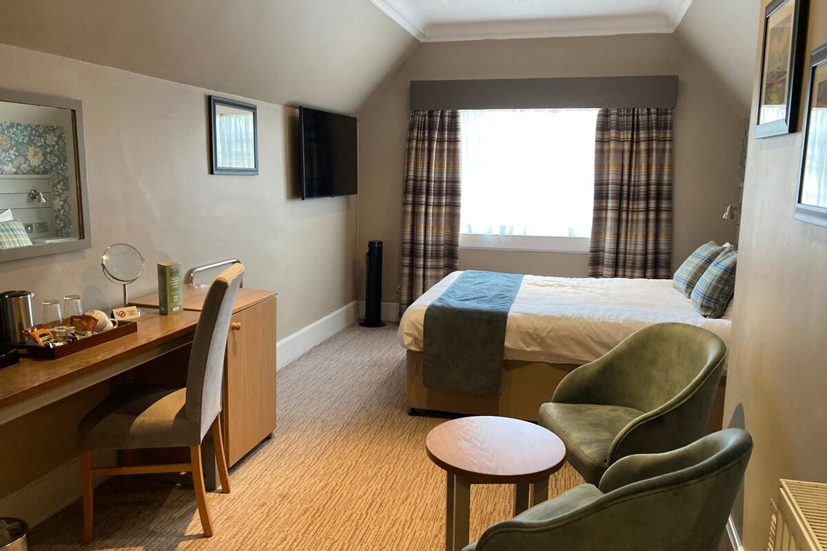 A hotel room with a bed, a desk with a chair, a small round table, and a television on the wall.