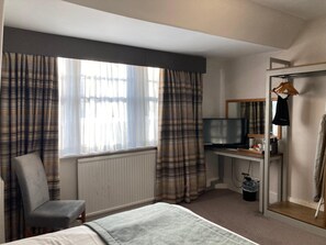 A hotel room with a bed, a chair, a desk with a television, a mirror, and a coat rack. - Tullie Inn (Alexandria)