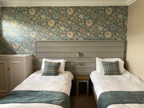 A hotel room with two beds, a wooden headboard, and floral wallpaper. - Tullie Inn (Alexandria)