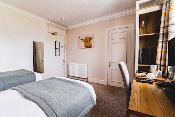 A hotel room with two beds, a desk with a chair, a radiator, and a door with a picture of a bull. - Tullie Inn (Alexandria)
