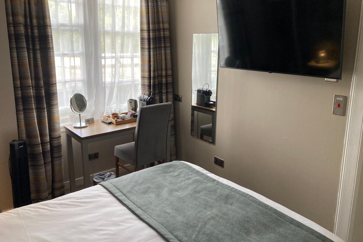 A hotel room with a bed, a desk with a chair, a television, and a window with curtains.