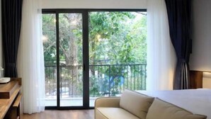 A modern hotel room with a sofa, a wooden desk, and a balcony with a view of greenery. - DD Hospitality - Mi Amor Da Lat (Xuan Huong - Da Lat)