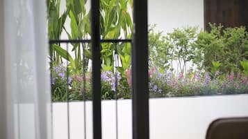 Vista a través de una ventana con reja metálica, mostrando follaje verde y flores púrpuras.