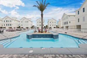 Una piscina con una palmera y solárium empedrado, rodeada de edificios blancos.