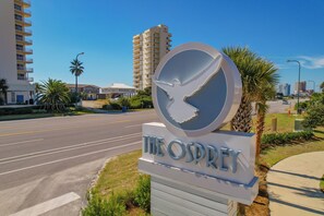 A sign for The Osprey hotel with a bird silhouette, a road, and buildings in the background. - Osprey 21 Osprey Sunshine by Kaiser Bayside Home Near the Beach & Community Pool (Orange Beach)