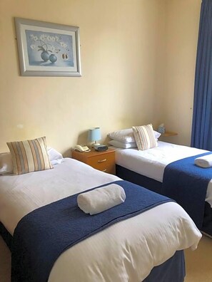 A hotel room with two beds, a nightstand with a lamp, a telephone, and a framed picture on the wall. - Green Tree Hotel (Peebles)
