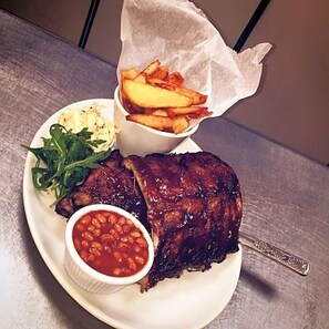 A plate with a grilled meat, a side of fries, a small bowl of beans, and a side salad. - Green Tree Hotel (Peebles)