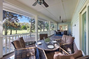 Eine überdachte Terrasse im Freien mit Korbmöbeln, einem Esstisch und Blick auf einen Golfplatz.