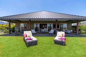 A covered outdoor seating area with two lounge chairs, a patio table, and a television screen. - 🏖️Starry Nights | 2 King Ensuites, Central AC & Sleeps 10 (Waikoloa)