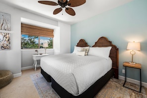 A bedroom with a large bed, a ceiling fan, a window with a view, a bedside table with a lamp, and a rug. - 🏖️Two King Ensuite Bedrooms + Pools & Hot Tubs (Kamuela)