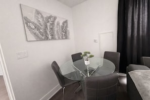 Moderni ruokailutila, jossa on lasipöytä, neljä tuolia, ruukkukasvi ja suuri abstrakti maalaus seinällä.
