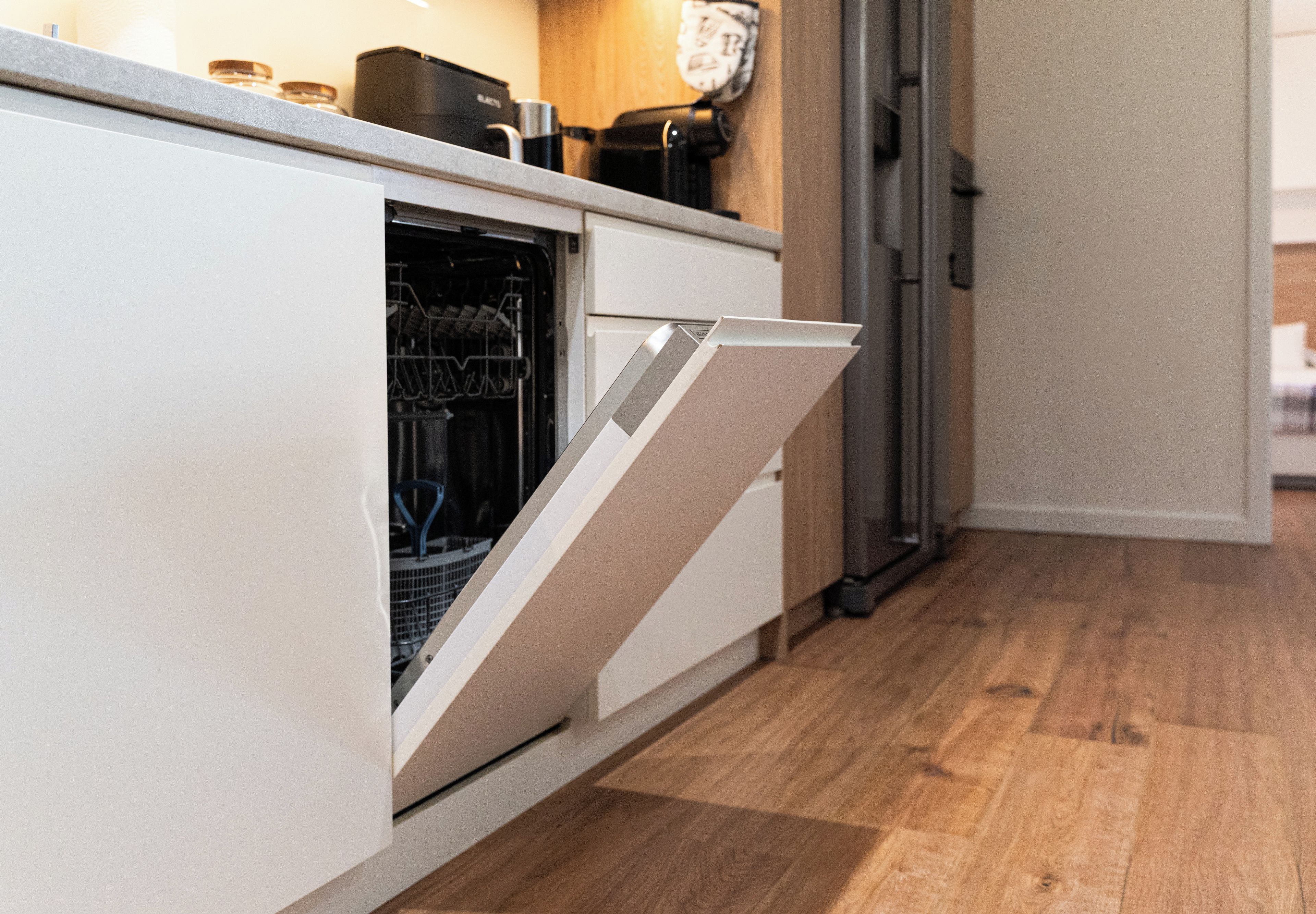 A kitchen with a dishwasher, wooden flooring, and a refrigerator.