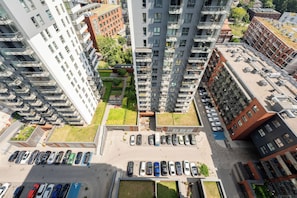 Ein Hochhaus mit mehreren Balkonen, einem Dachgarten und einem Parkplatz mit Autos.