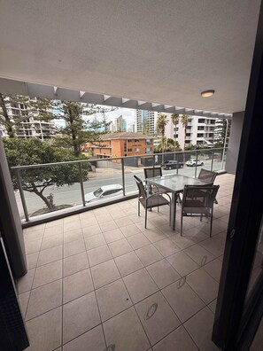 A balcony with a glass table and chairs, overlooking a street with cars and buildings. - 2 Bedroom Hideaway (Surfers Paradise)