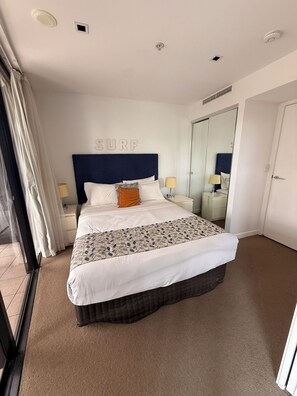 Ett hotellrum med en stor säng, en sänggavel med ordet ”SURF” på, två sängbord med lampor, en stor spegel och en dörr.