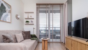 A modern living room with a sofa, a small table, a TV on a wooden stand, and a sliding glass door leading to a balcony. - Łódź Fabryczna Signature Apartment (Łódź)