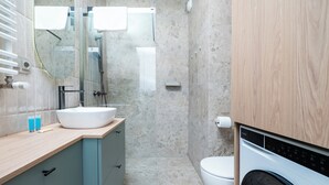 A modern bathroom with a sink, mirror, toilet, and a washing machine. - Łódź Fabryczna Signature Apartment (Łódź)