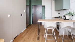 A modern kitchen with a wooden countertop, two white bar stools, and a view into a dining area. - Łódź Fabryczna Signature Apartment (Łódź)