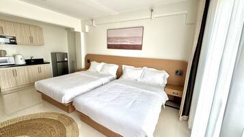A hotel room with two beds, a kitchenette, and a view of the beach.