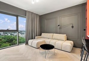 Ein modernes Wohnzimmer mit einer Eckcouch, einem runden schwarzen Couchtisch und Blick auf eine Skyline durch große Fenster.