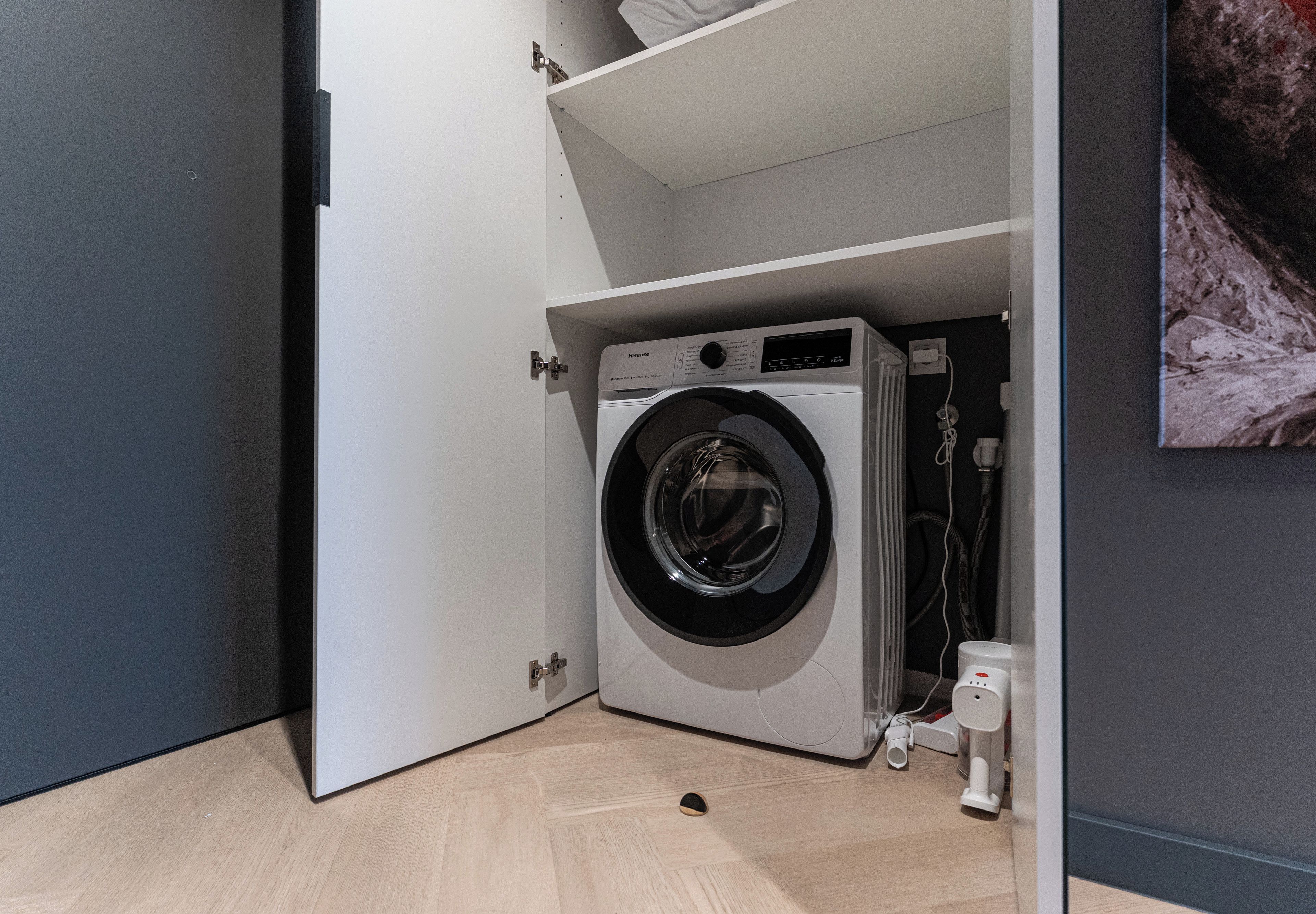Ein kleiner Hauswirtschaftsraum mit einer Waschmaschine mit Frontlader, einem Wäscheständer und einem kleinen Regal darüber.