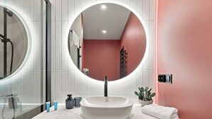 Bany amb un mirall rodó, un lavabo de marbre blanc i una paret amb detall vermell.