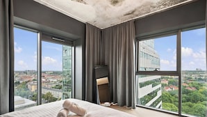 Habitació d'hotel amb un llit gran, vista a la ciutat i un edifici modern a l'altre costat del carrer.