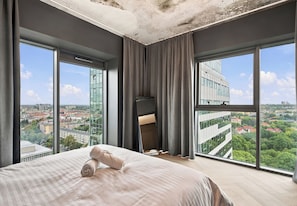Ein Hotelzimmer mit einem großen Bett, Blick auf die Stadt und einem modernen Gebäude gegenüber.