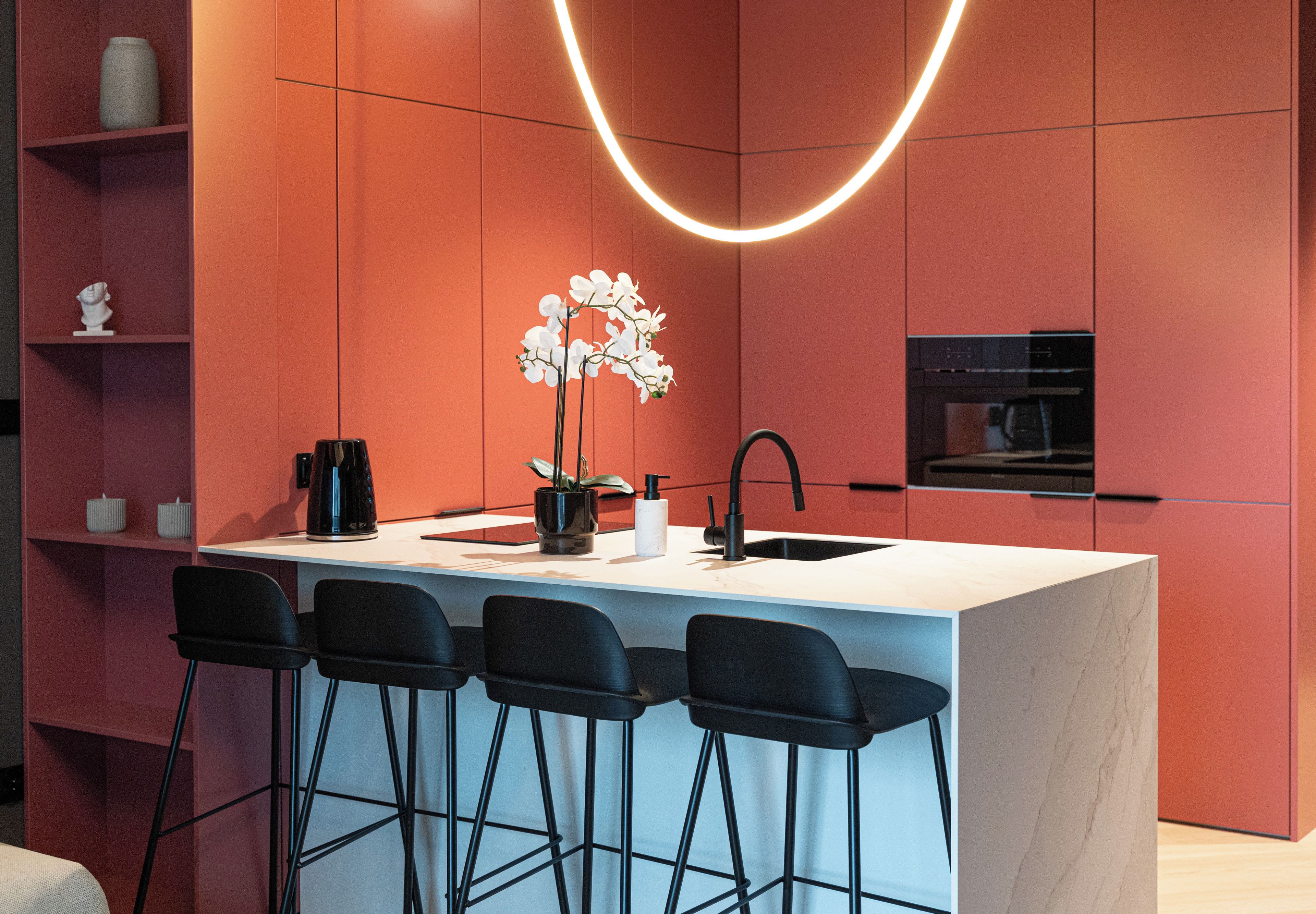 A modern kitchen with a central island, bar stools, a sink, and a built-in oven.