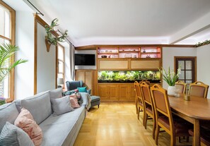 A living room with a sofa, a dining table with chairs, a television, and a fish tank. - Piwna Old Town Residence Apartment (Warszawa)
