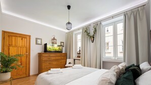 Ein Hotelzimmer mit Holzschrank, einem Bett mit weißen Leinen, einer Topfpflanze und einem Fernseher auf einer Holzkombination.