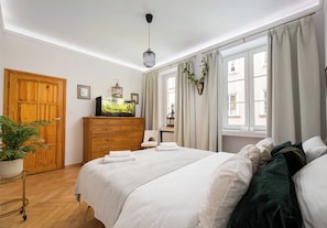 A hotel room with a wooden wardrobe, a bed with white linens, a potted plant, and a television on a wooden dresser. - Piwna Old Town Residence Apartment (Warszawa)