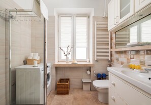 A modern bathroom with a Bosch washing machine, a toilet, a wicker basket, and a window with blinds. - Piwna Old Town Residence Apartment (Warszawa)