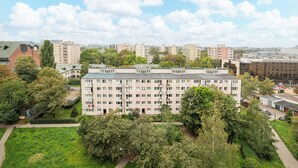 Ein mehrgeschossiges Wohngebäude mit flachem Dach, umgeben von Grünflächen und weiteren Gebäuden.