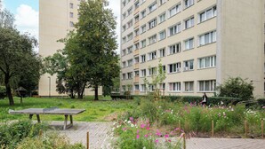 Ein Park mit einer Steinsitzbank, blühenden Pflanzen und einem hohen Gebäude im Hintergrund.