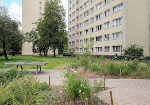 A park with a stone bench, flowering plants, and a tall building in the background. - Metro Wierzbno Homely Apartment (Warszawa)