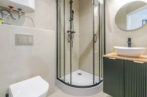 A modern bathroom with a glass-enclosed shower, a white toilet, a sink with a bowl, and a mirror. - Krzywa Central Studio (Katowice)