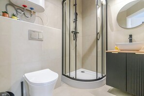 Et moderne badeværelse med en glasafskærmet bruseniche, et hvidt toilet og en vaskebord med vask.