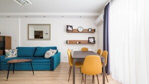 Ein modernes Wohnzimmer mit einem blauen Sofa, einem Holztisch und einem Essbereich mit Tisch und gelben Stühlen.